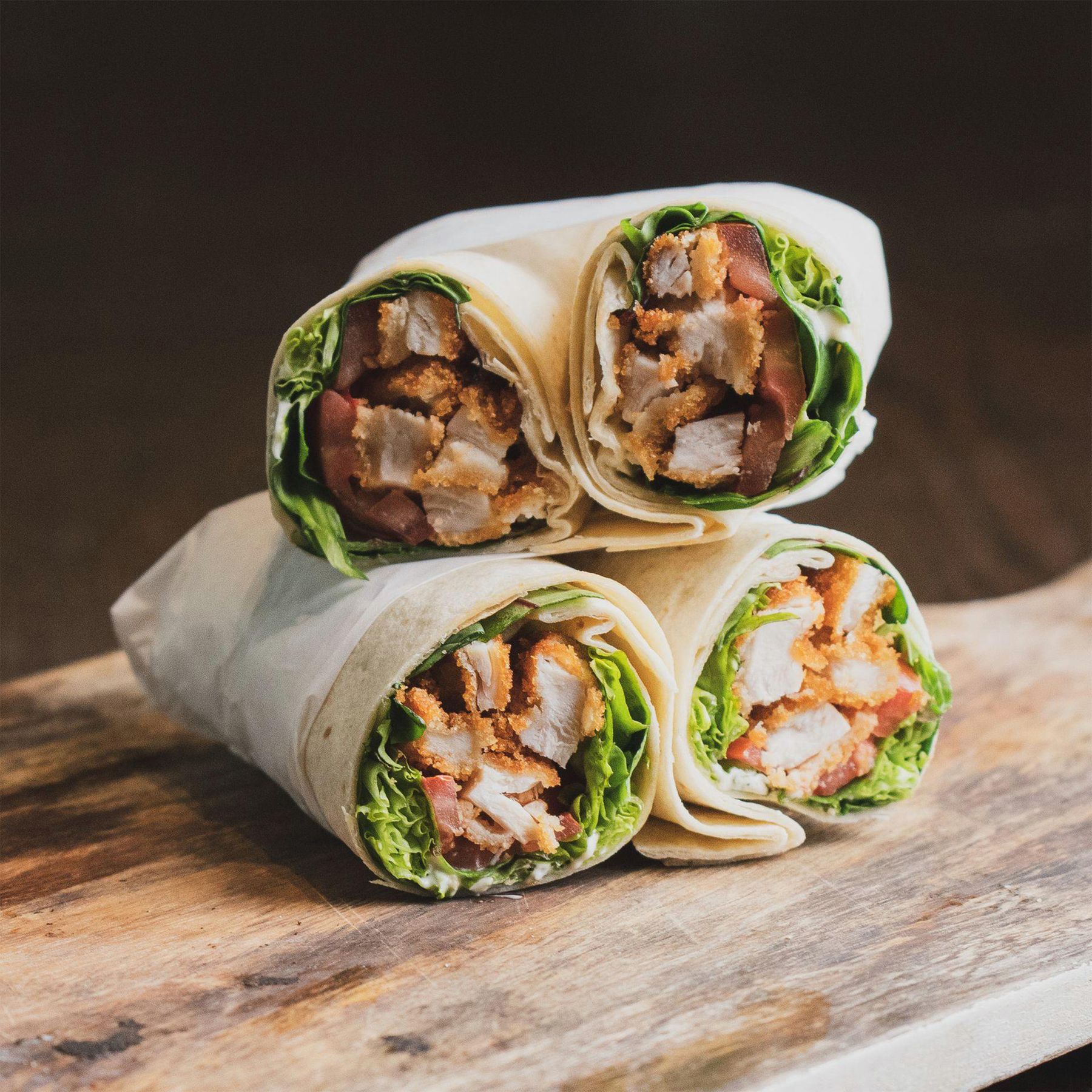Chicken wraps stacked on a wooden board